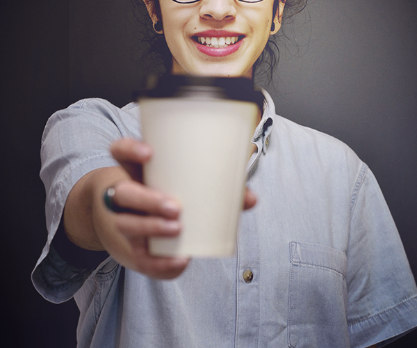 A smiling woman handing out a cup of coffee